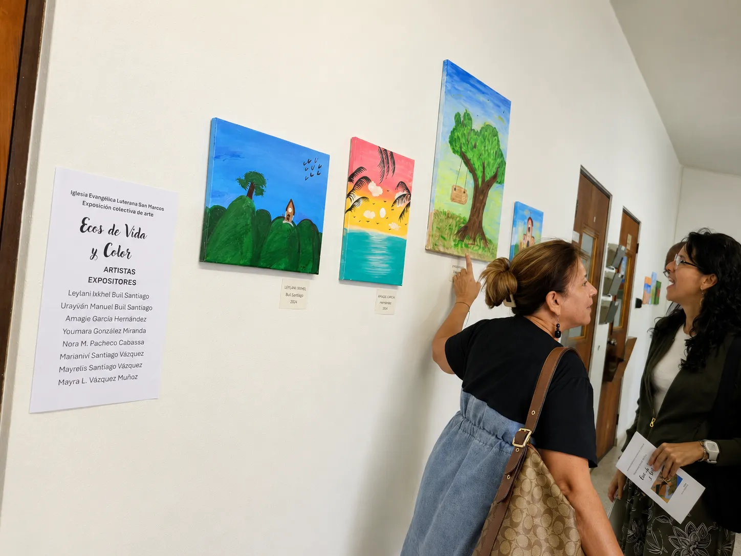 Personas conversan frente a las pinturas presentadas en Ecos de Vida y Color