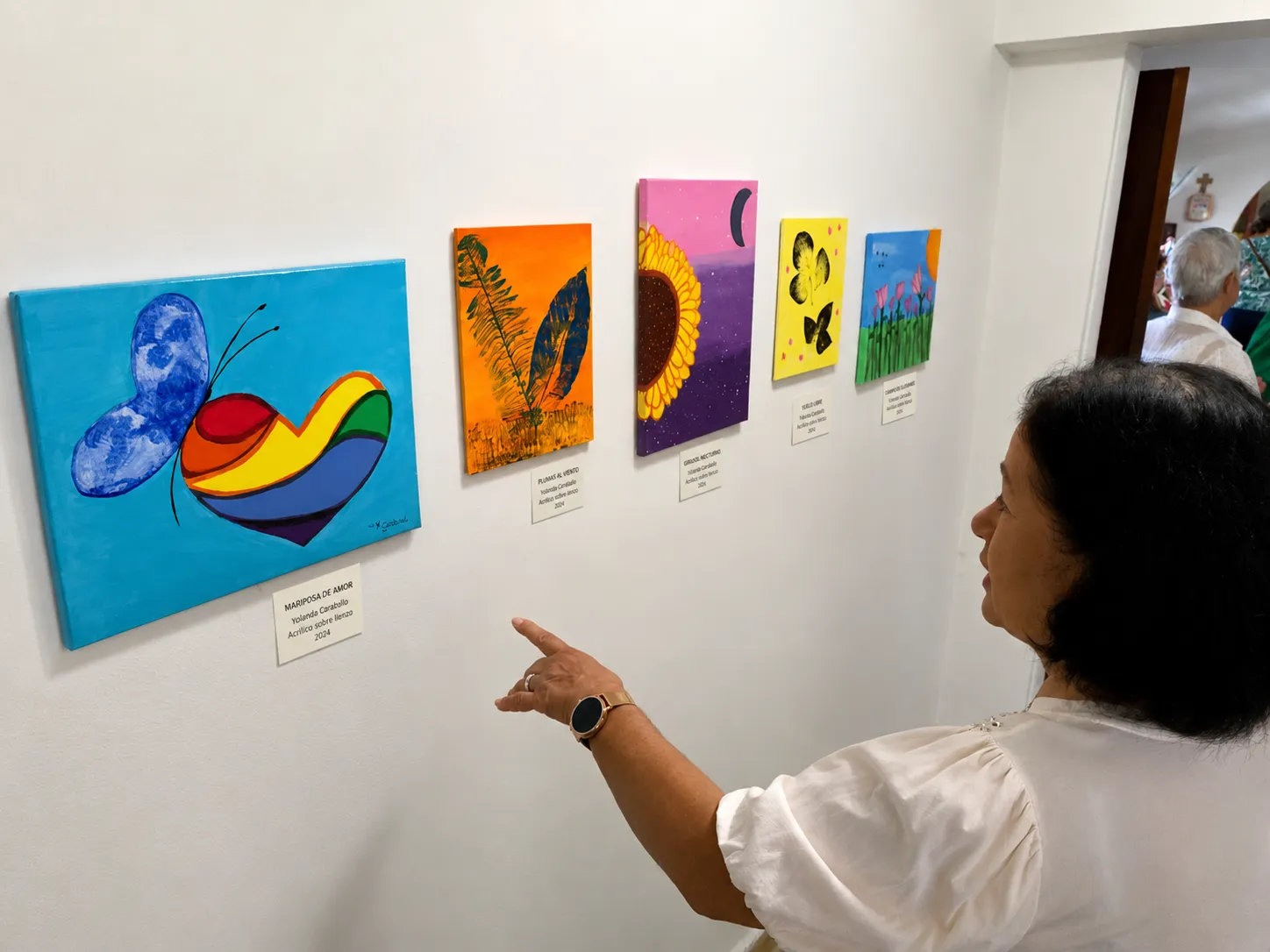 Una visitante contempla y señala varias obras de la exposición Ecos de Vida y Color